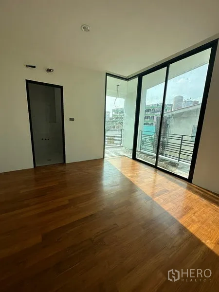 Detached House for rent in Watthana, Bangkok - Bright bedroom with wooden floors and sliding doors opening to a balcony over the neighborhood.