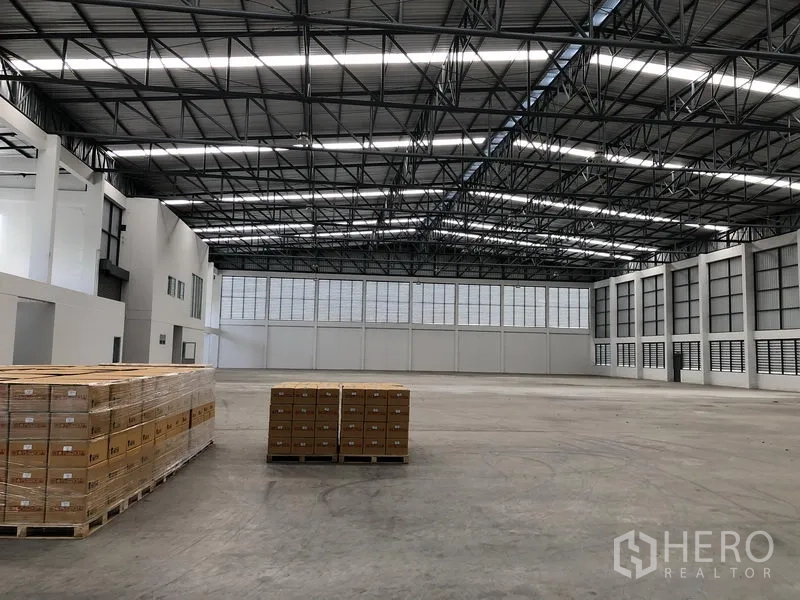 Factory for rent in Phra Nakhon Si Ayutthaya - Open warehouse floor with stacked pallets beneath a skylit steel truss roof.