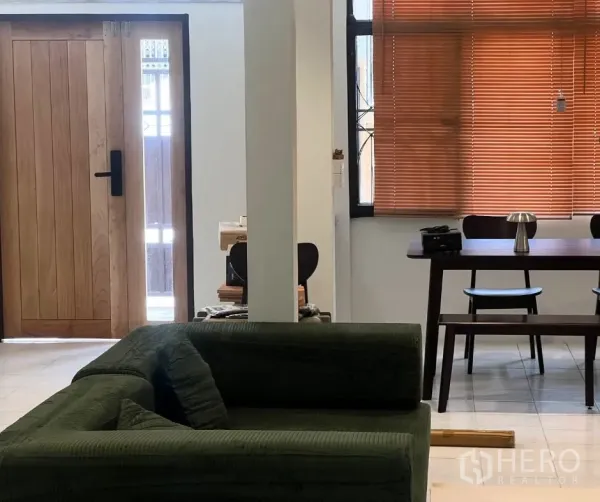 Townhouse for rent - Open‑plan living and dining with a green sofa, wooden entrance door and window blinds.