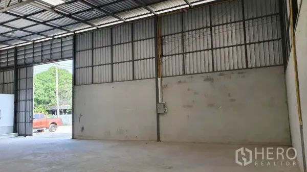 Warehouse for rent in Pathum Thani - High-ceiling steel-frame warehouse interior with concrete floor and wide loading door.