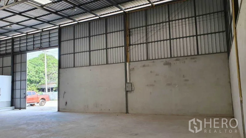 Warehouse for rent in Pathum Thani - High-ceiling steel-frame warehouse interior with concrete floor and wide loading door.
