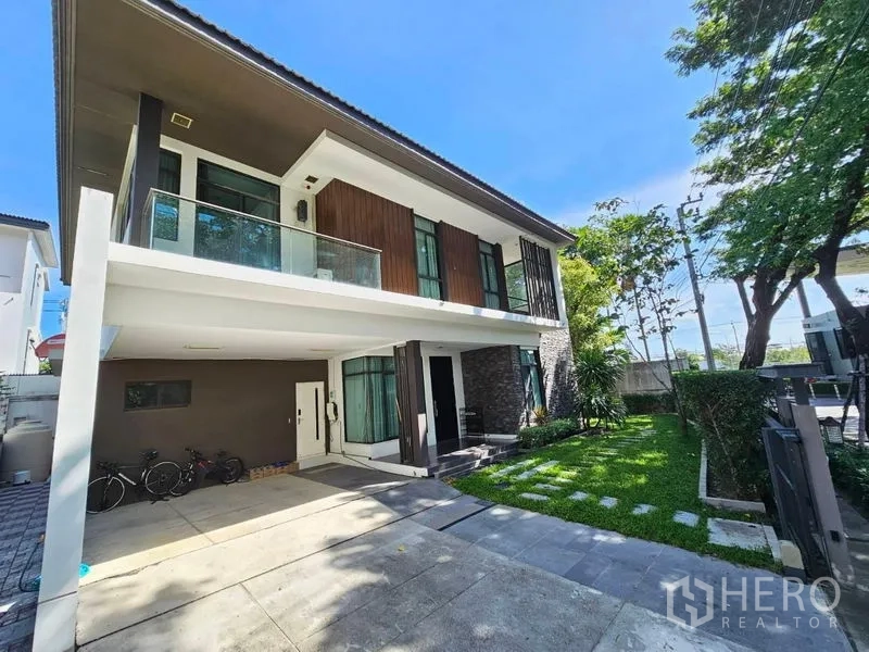 Detached House for sale in Prawet, Bangkok - Angled front view of the house with balcony, stone cladding and green garden.