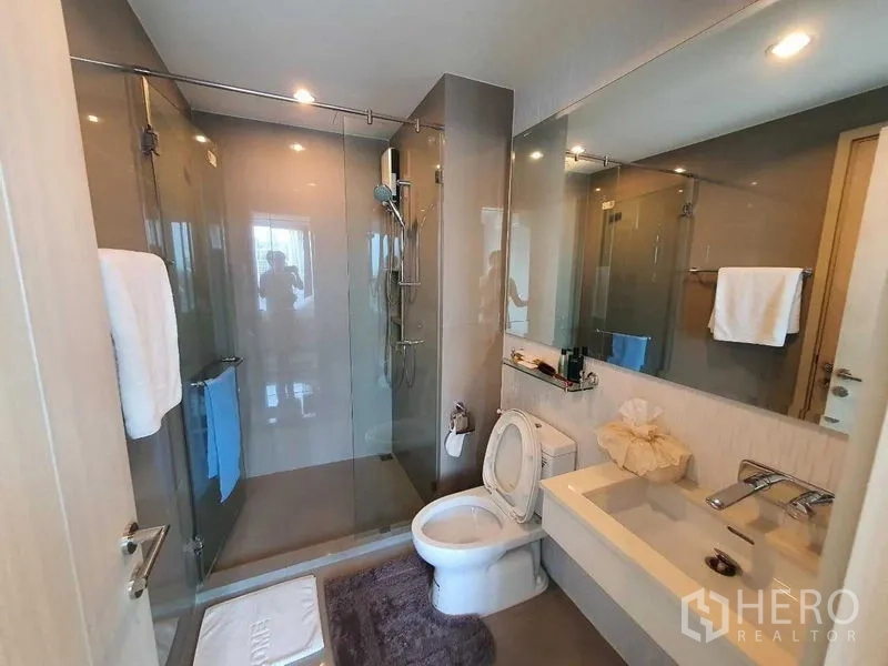 Condominium for sale in Khlong Toei, Bangkok - Modern bathroom featuring a glass-enclosed shower, large mirror, and vanity.