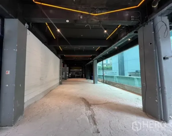 Retail Space for rent - Shell unit corridor view showing floor-to-ceiling glazing, feature lighting and structural columns along one wall.