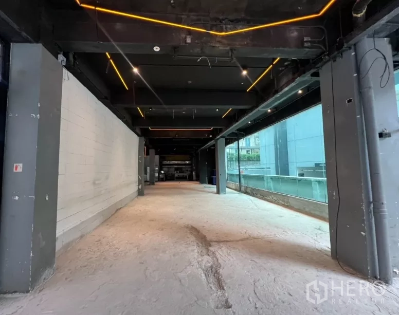 Retail Space for rent - Shell unit corridor view showing floor-to-ceiling glazing, feature lighting and structural columns along one wall.