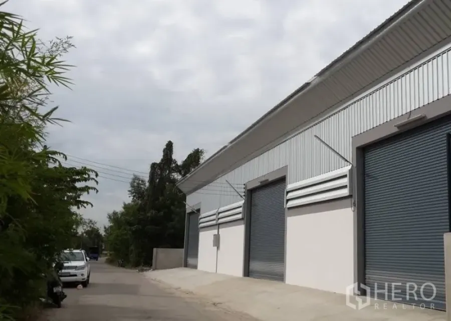 货栈 出租在Nonthaburi - 仓库外观，金属板立面与多樘卷闸门，临安静小路。