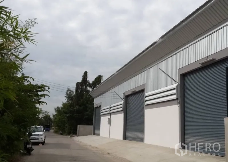 货栈 出租在Nonthaburi - 仓库外观，金属板立面与多樘卷闸门，临安静小路。