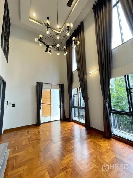 Detached House for rent in Bang Na, Bangkok - Double-height room with statement chandelier, tall curtains and balcony doors.