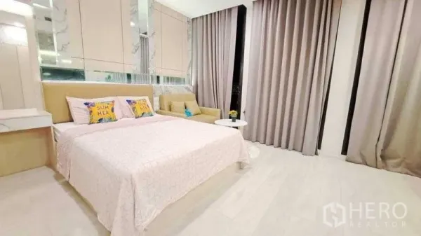 Condominium for sale in Pathum Wan, Bangkok - Cozy sleeping area with bed, side vanity, soft grey drapes, light floors and a sofa corner.