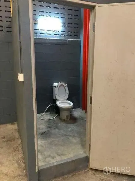 Factory for rent in Phra Pradaeng, Samut Prakan - Simple restroom with toilet inside the factory building with concrete walls and floor.