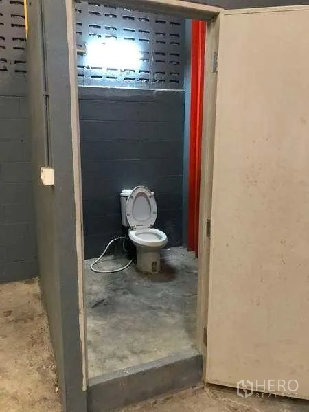 Factory for rent in Phra Pradaeng, Samut Prakan - Simple restroom with toilet inside the factory building with concrete walls and floor.