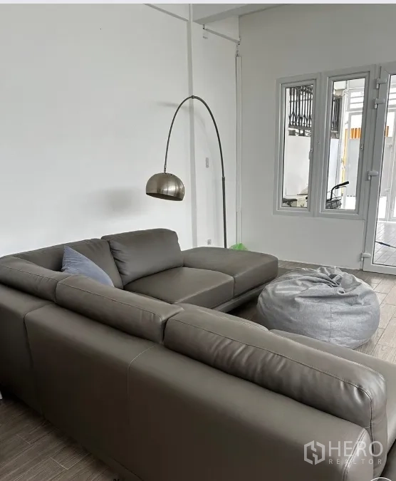 Townhouse for rent in Sathon, Bangkok - Cozy living area with gray sectional sofa, floor lamp, and windows.