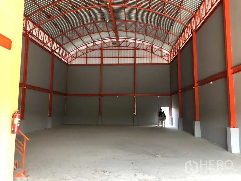 Warehouse for rent in Nonthaburi - Spacious warehouse interior with high arched steel roof, red trusses and clear open floor suitable for storage or light production.