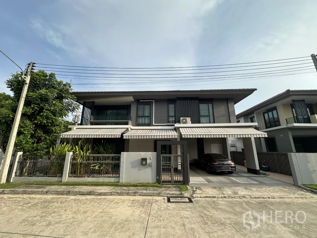 Detached House for rent or sale in Lam Luk Ka, Pathum Thani - Modern two-storey detached house with gated fence, striped awnings and a covered two-car carport on a quiet street in Lam Luk Ka.