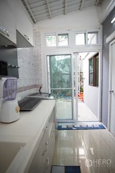 Townhouse for rent in Suan Luang, Bangkok - Kitchen view toward sliding glass doors opening to a small patio with plants.