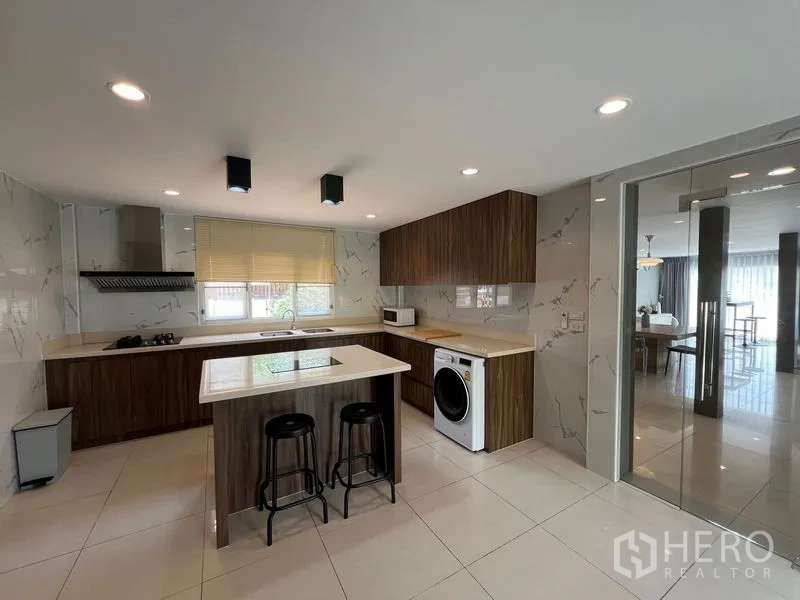 Detached House for sale in Mueang Pathum Thani, Pathum Thani - Full view of L-shaped kitchen with island, induction hob and glass door to dining.
