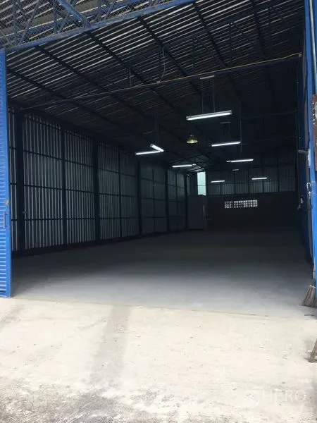 Warehouse for rent in Bang Kapi, Bangkok - Open warehouse interior in Bang Kapi, Bangkok with high steel roof, bright strip lighting and smooth concrete floor behind blue roller doors.