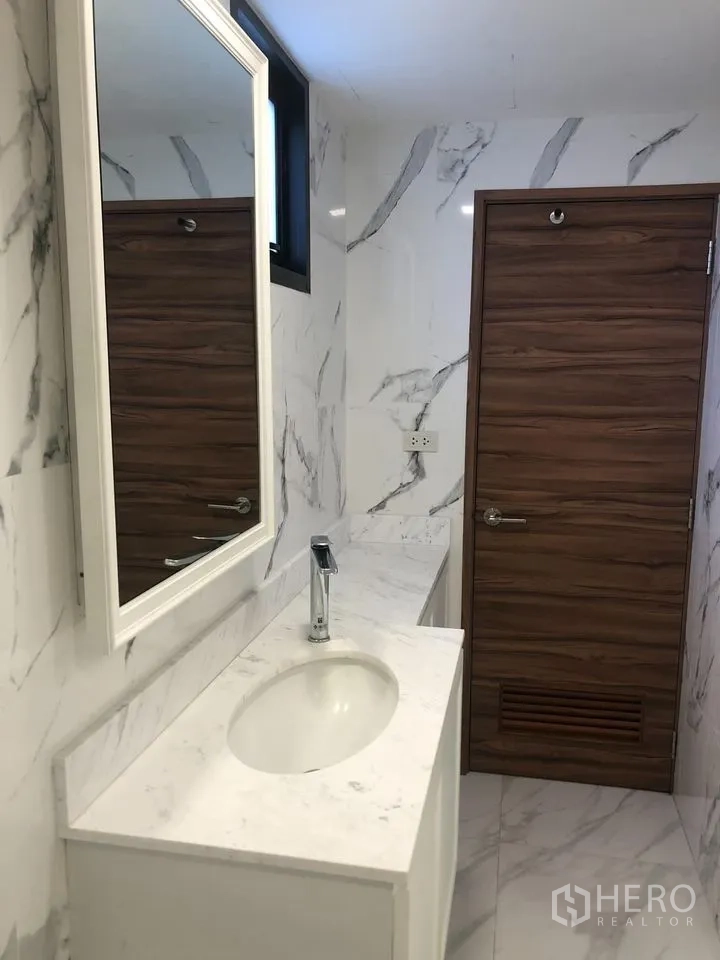 Detached House for rent in Khlong Toei, Bangkok - Secondary bathroom with marble walls, white vanity and wooden door