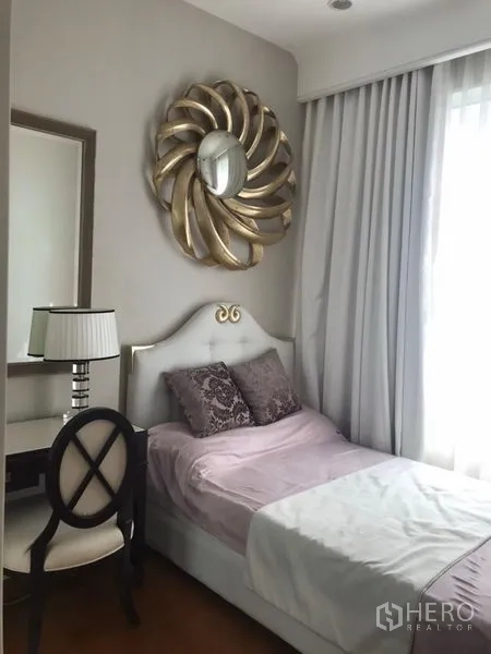 Condominium for rent in Pathum Wan, Bangkok - Cozy secondary bedroom with single bed, vanity desk and chair, large decorative wall mirror and soft drapes.