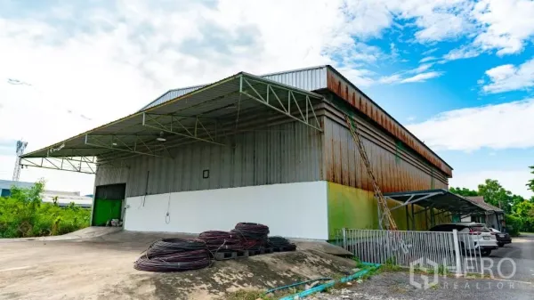 Warehouse for rent in Thanyaburi, Pathum Thani - Side view of the warehouse showing a concrete driveway slope, steel canopy, large roller door and ample yard space.