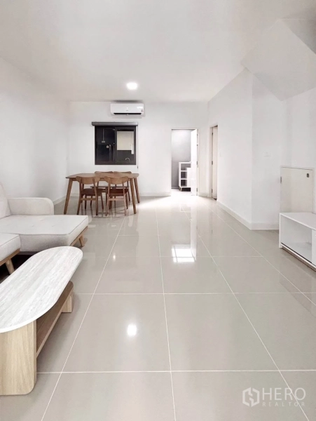Townhouse for rent in Bang Phli, Samut Prakan - Long open living zone with sofa, dining table, air conditioning and doorway to the kitchen.