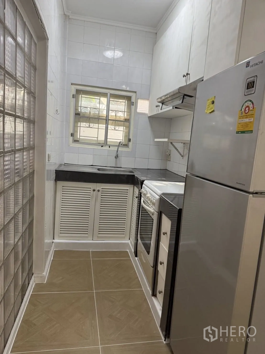 Detached House for rent in Khlong Toei, Bangkok - Compact fitted kitchen with cabinets, stove and oven, range hood, refrigerator, and sink.