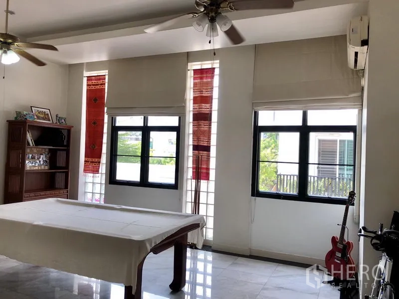 Townhouse for rent or sale in Bangkok - Bright multipurpose room with multiple windows, ceiling fans and a table, plus guitar and shelving.