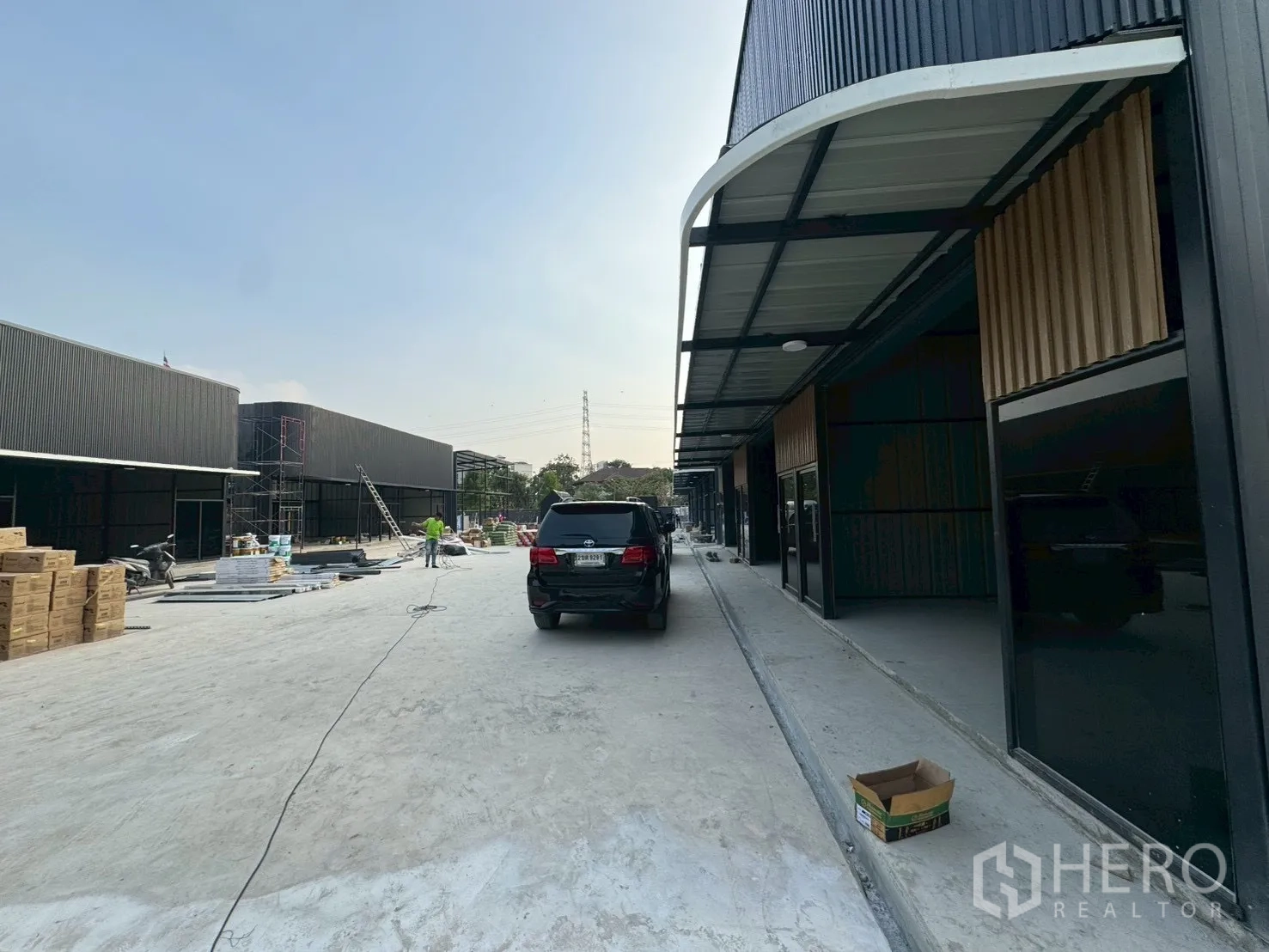 Warehouse for rent in Suan Luang, Bangkok - Modern black-clad warehouse units with covered loading bays along a wide concrete driveway and parked car.