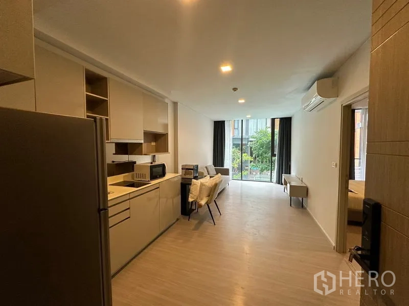 Condominium for rent in Khlong Toei, Bangkok - Open-plan kitchen and living area with dining set, large windows, and greenery outlook in a Bangkok condominium.