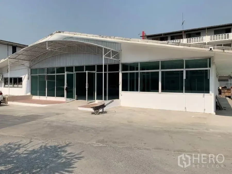 Warehouse for rent in Mueang Pathum Thani, Pathum Thani - Warehouse exterior with white facade, glass front, steel canopy and wide concrete yard for parking.