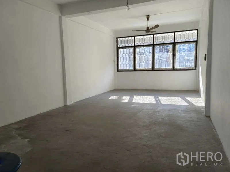 Shophouse for rent in Bang Na, Bangkok - Bright upper-floor room with large grilled windows and a ceiling fan.