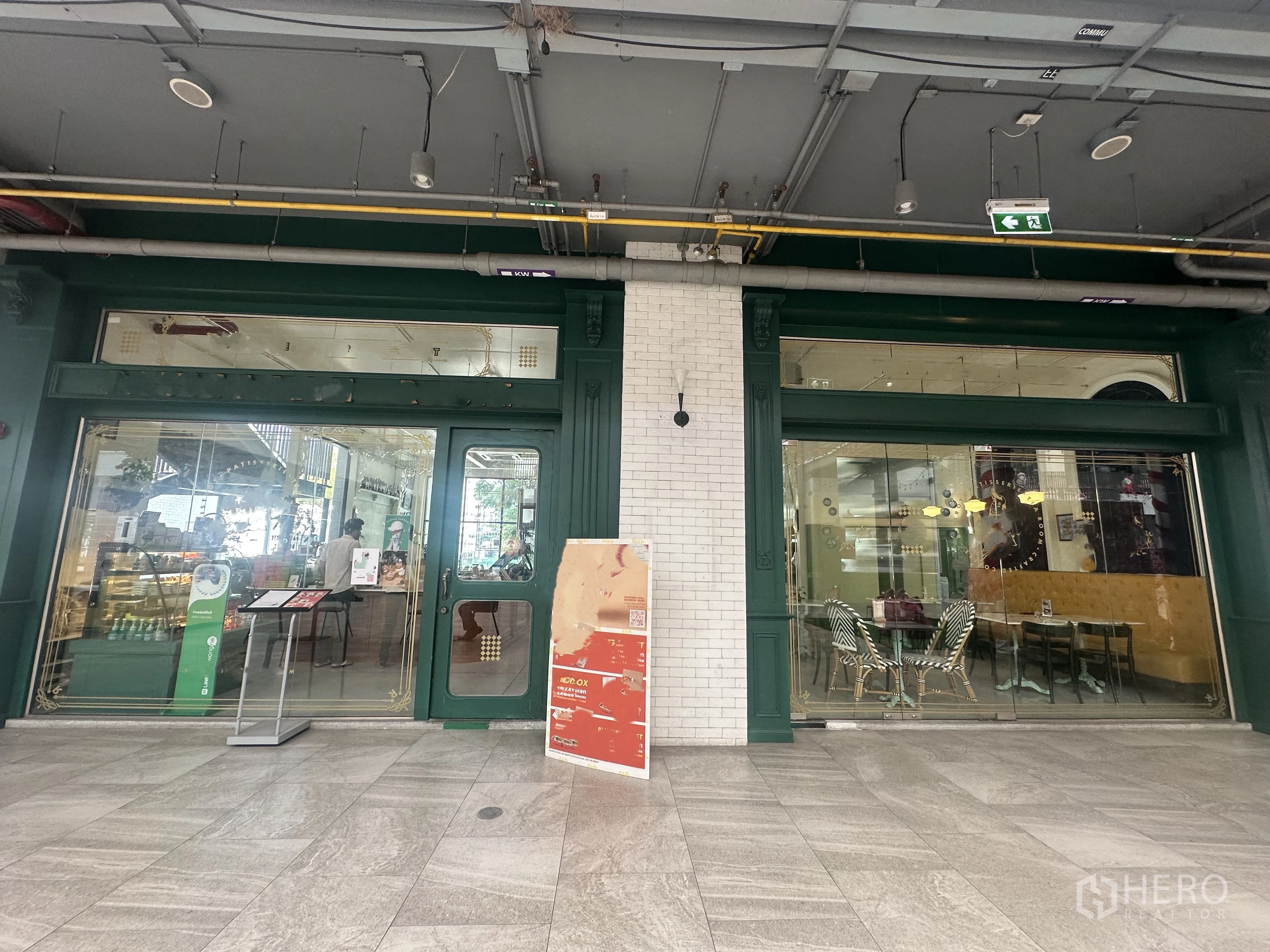 Retail Space for sale in Khlong Toei, Bangkok - Green-framed glass storefront with double doors, large display windows, and polished stone walkway inside a covered retail arcade.