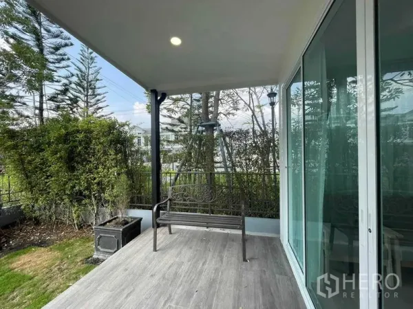 Townhouse for rent or sale in Prawet, Bangkok - Covered patio with metal bench overlooking a green garden and sliding glass doors.