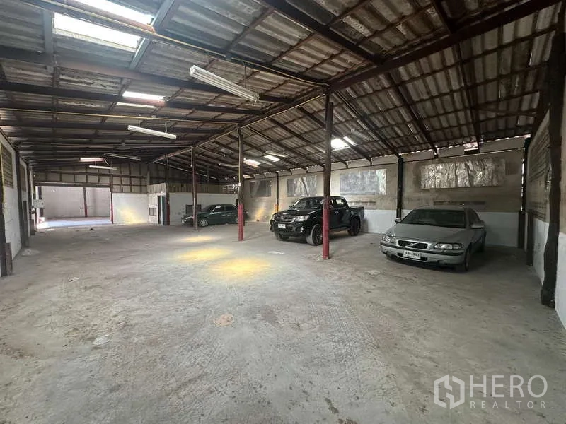 Warehouse for rent in Suan Luang, Bangkok - Wide-span storage hall with skylights, red steel columns and cars positioned near the walls.