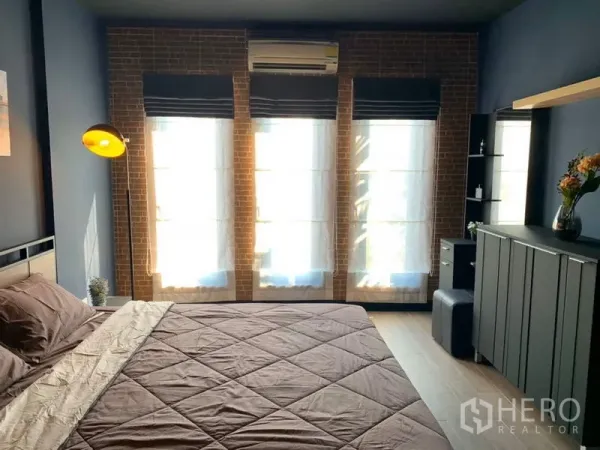 Townhouse for rent in Bang Kapi, Bangkok - Primary bedroom with brick accent wall, tall windows and air conditioning.