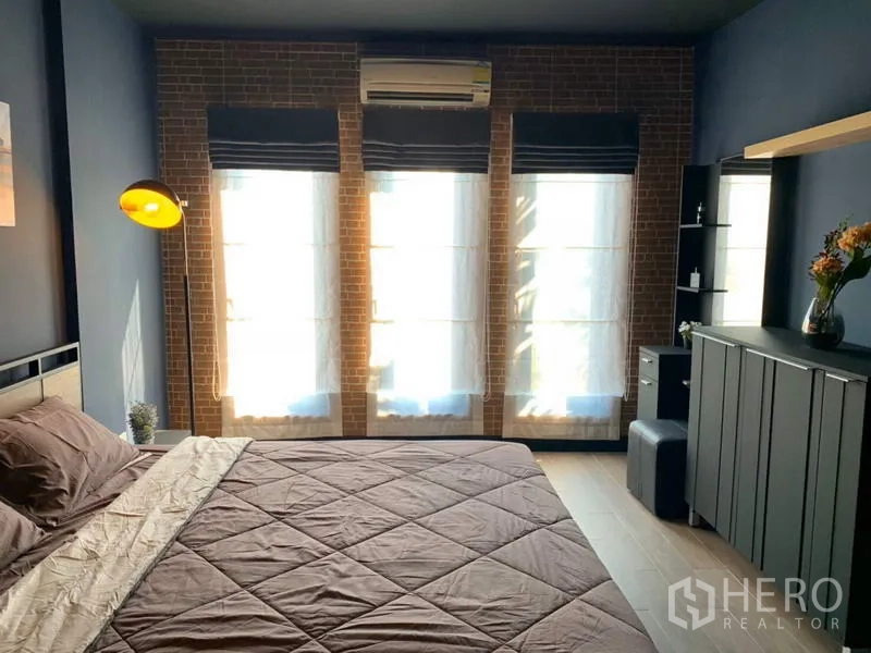 Townhouse for rent in Bang Kapi, Bangkok - Primary bedroom with brick accent wall, tall windows and air conditioning.