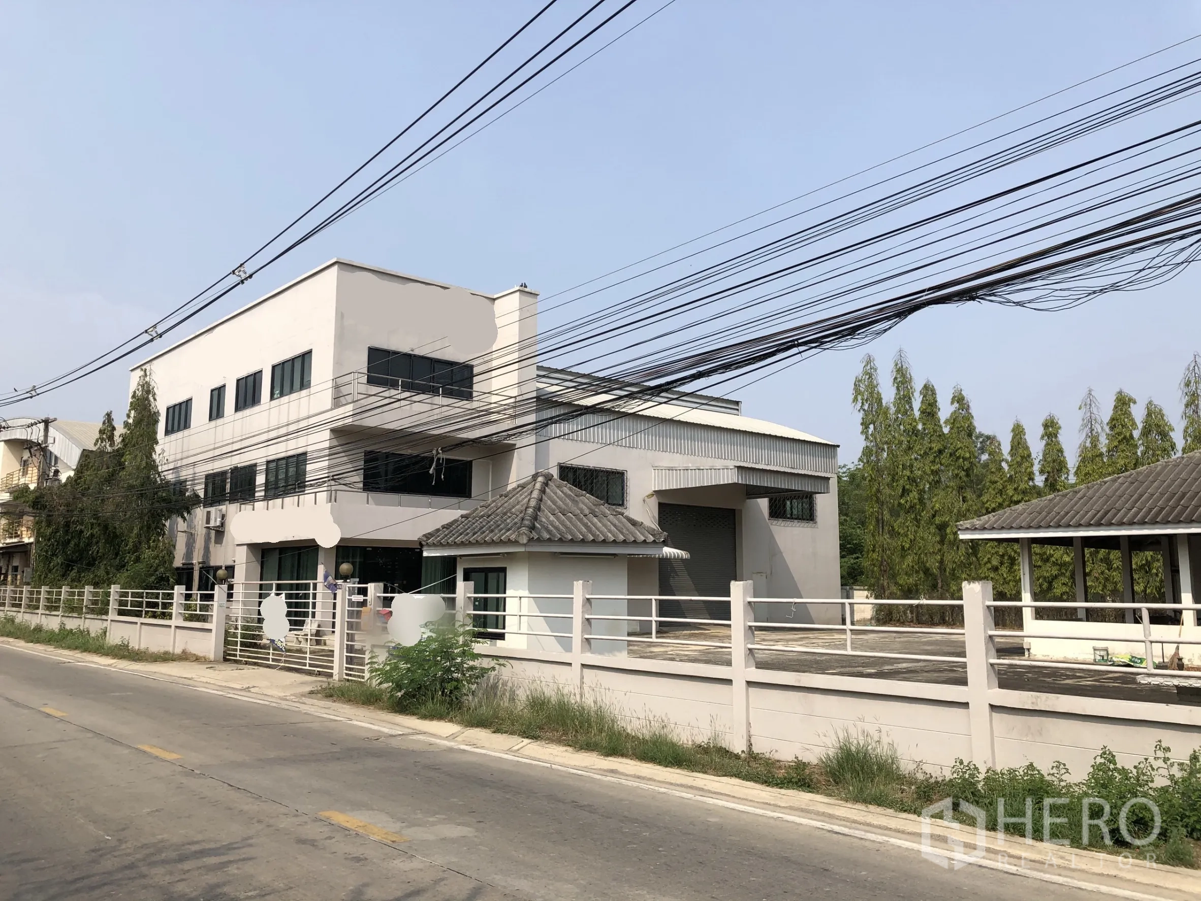 Factory for sale in Lam Luk Ka, Pathum Thani - Front view of a modern factory with office wing, loading bay and gated perimeter along a quiet road.
