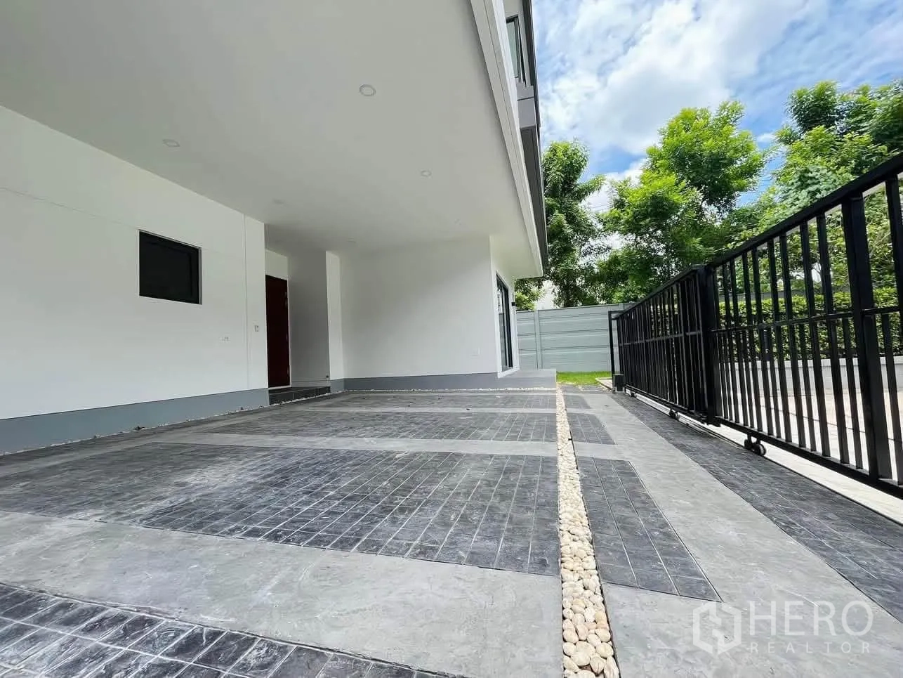Detached House for rent or sale in Prawet, Bangkok - Covered carport with gated driveway and a strip of lawn and trees along the fence.