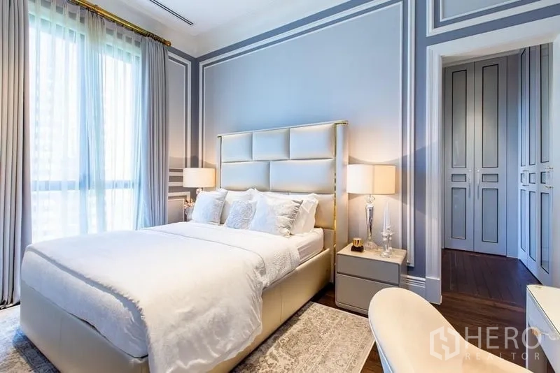 Condominium for sale in Pathum Wan, Bangkok - Second bedroom with padded headboard, soft grey walls and floor-to-ceiling drapes.