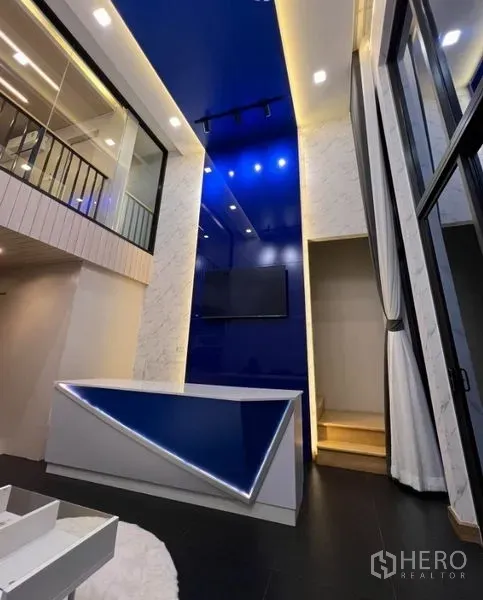 Townhouse for rent in Thanyaburi, Pathum Thani - Double-height living area with blue feature wall, LED-lit counter, and mezzanine glass railing.