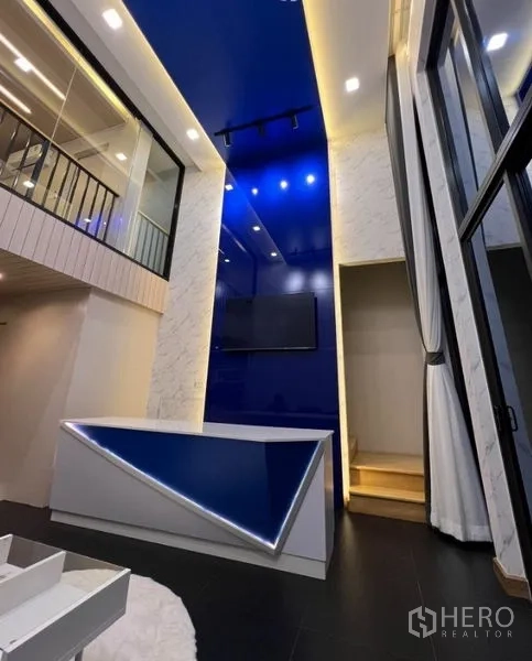 Townhouse for rent in Thanyaburi, Pathum Thani - Double-height living area with blue feature wall, LED-lit counter, and mezzanine glass railing.