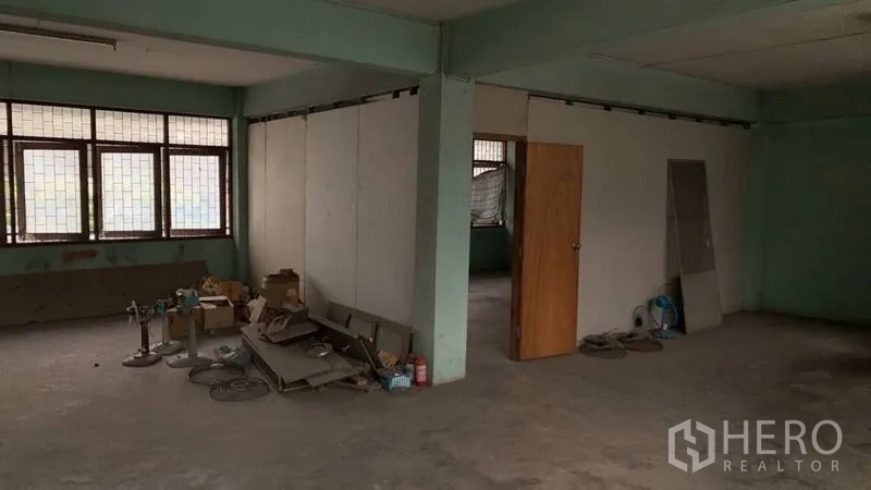 Shophouse for sale in Khlong Toei, Bangkok - Spacious upper level with partitioned room, grid windows and raw concrete floors.
