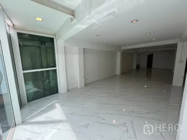 Retail Space for rent in Khlong Toei, Bangkok - Long showroom area with recessed ceiling lights, white walls and a glass lift enclosure near the entrance.