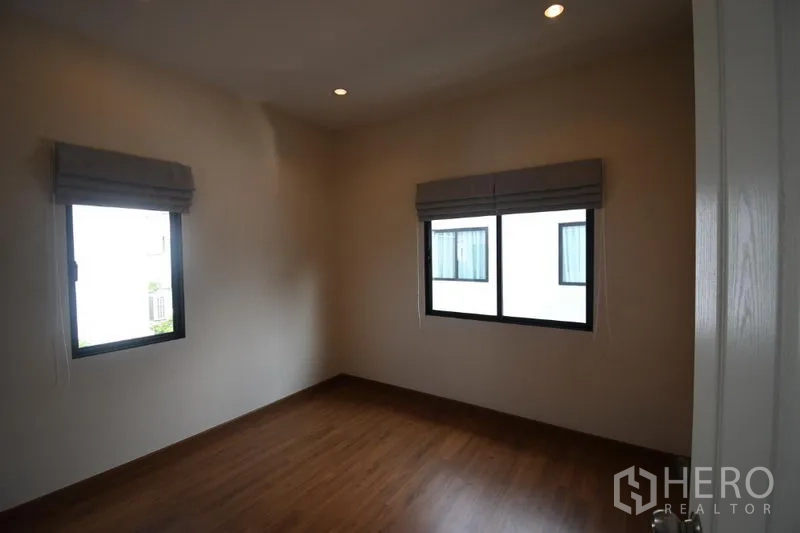 Detached House for rent in Prawet, Bangkok - Secondary bedroom with two windows, wood floors, and roman blinds.