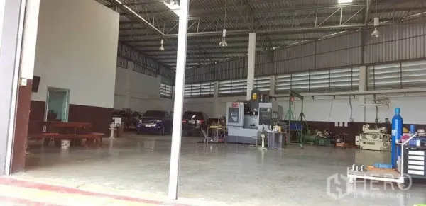 Factory for sale in Bang Phli, Samut Prakan - Spacious factory floor with high ceiling, CNC machine and parked vehicles inside a well‑ventilated warehouse.