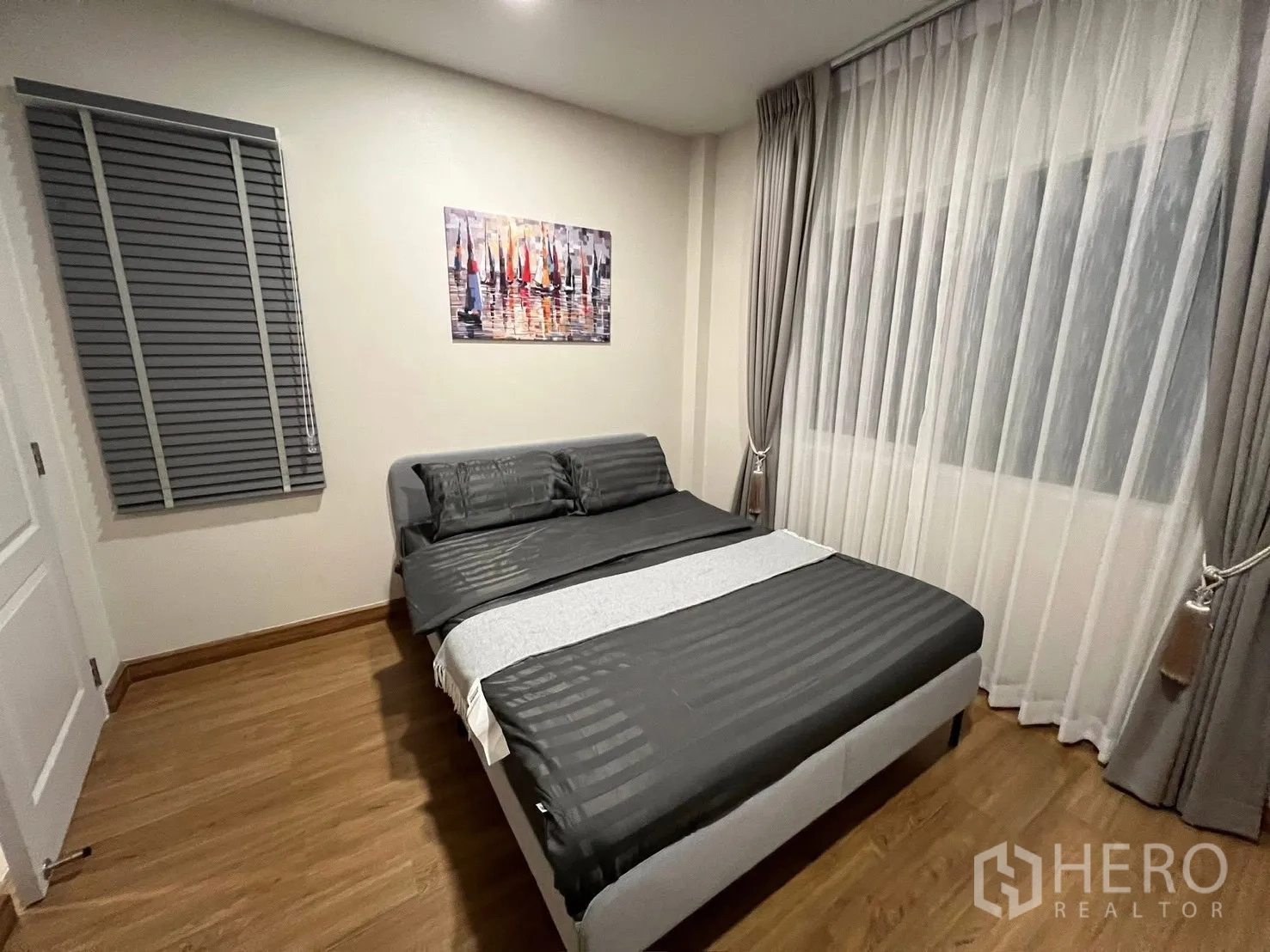 Detached House for rent in Prawet, Bangkok - Guest bedroom with bed, artwork on the wall and sheer drapes beside a window blind.