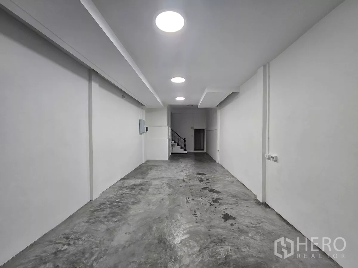 Shophouse for rent in Watthana, Bangkok - Bright concrete‑floor hall with recessed lighting and a staircase at the back.
