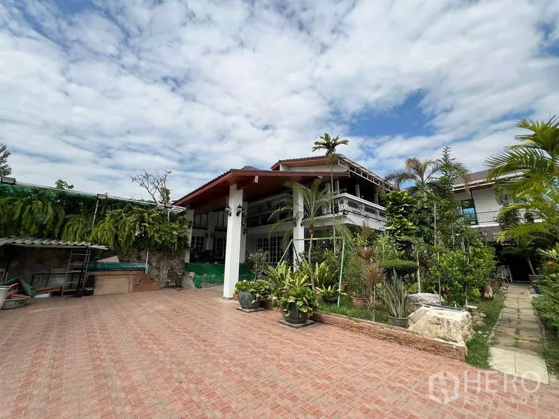 Detached House for rent in Chatuchak, Bangkok - Two-storey detached house in Chatuchak with a wide tiled driveway and tropical garden under blue sky.
