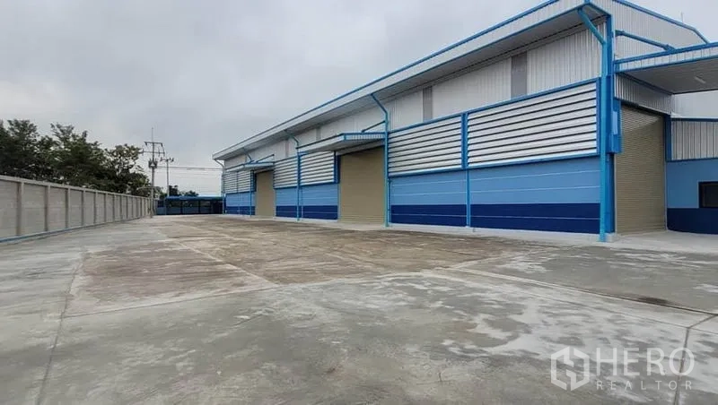 Factory for rent or sale in Phanat Nikhom, Chon Buri - Long concrete driveway alongside the warehouse with roller shutter loading doors.