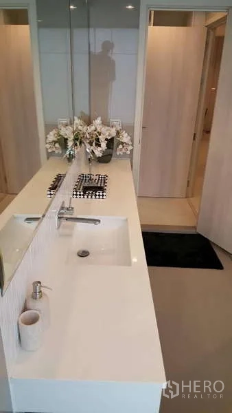 Condominium for rent in Khlong Toei, Bangkok - Bathroom vanity with long countertop, under-mount sink and large mirror.